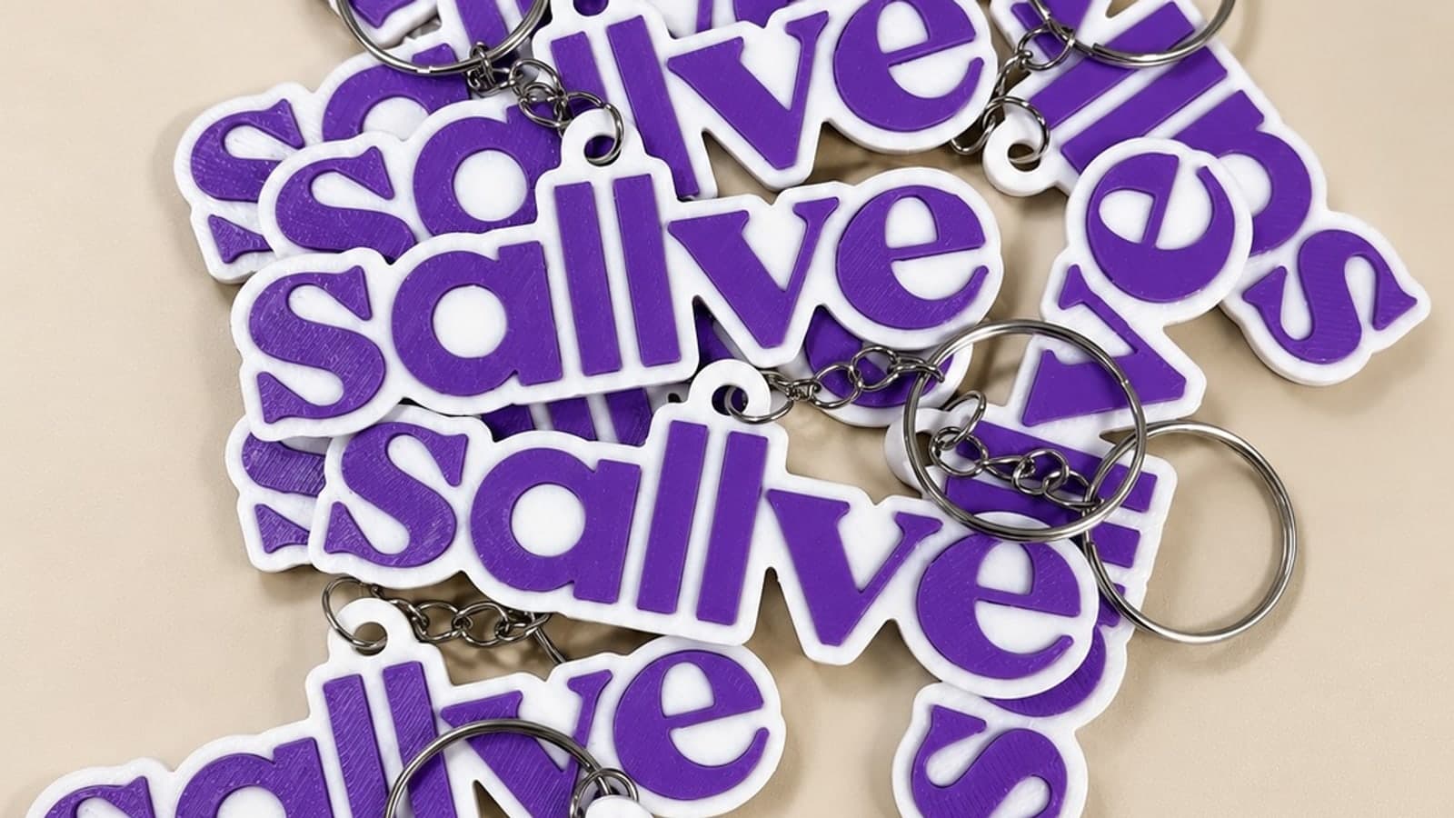 Chaveiros brancos com o logo roxo de uma marca de cosméticos, impressos em 3D, espalhados sobre a bancada da oficina