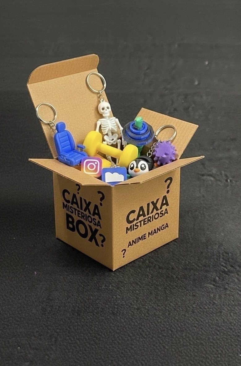 Caixa de papelão escrita “Caixa misteriosa” aberta, cheia de chaveiros e miniaturas coloridas impressas em 3D